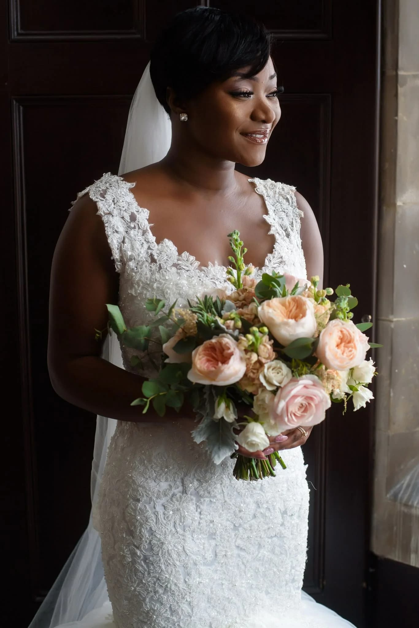 Bride holding a peach and cream bouquet by a doorway