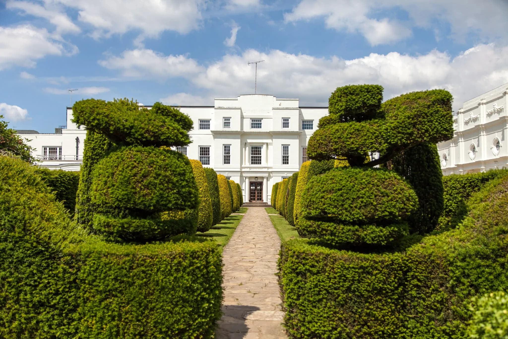 Topiary-lined path leading to a white manor house